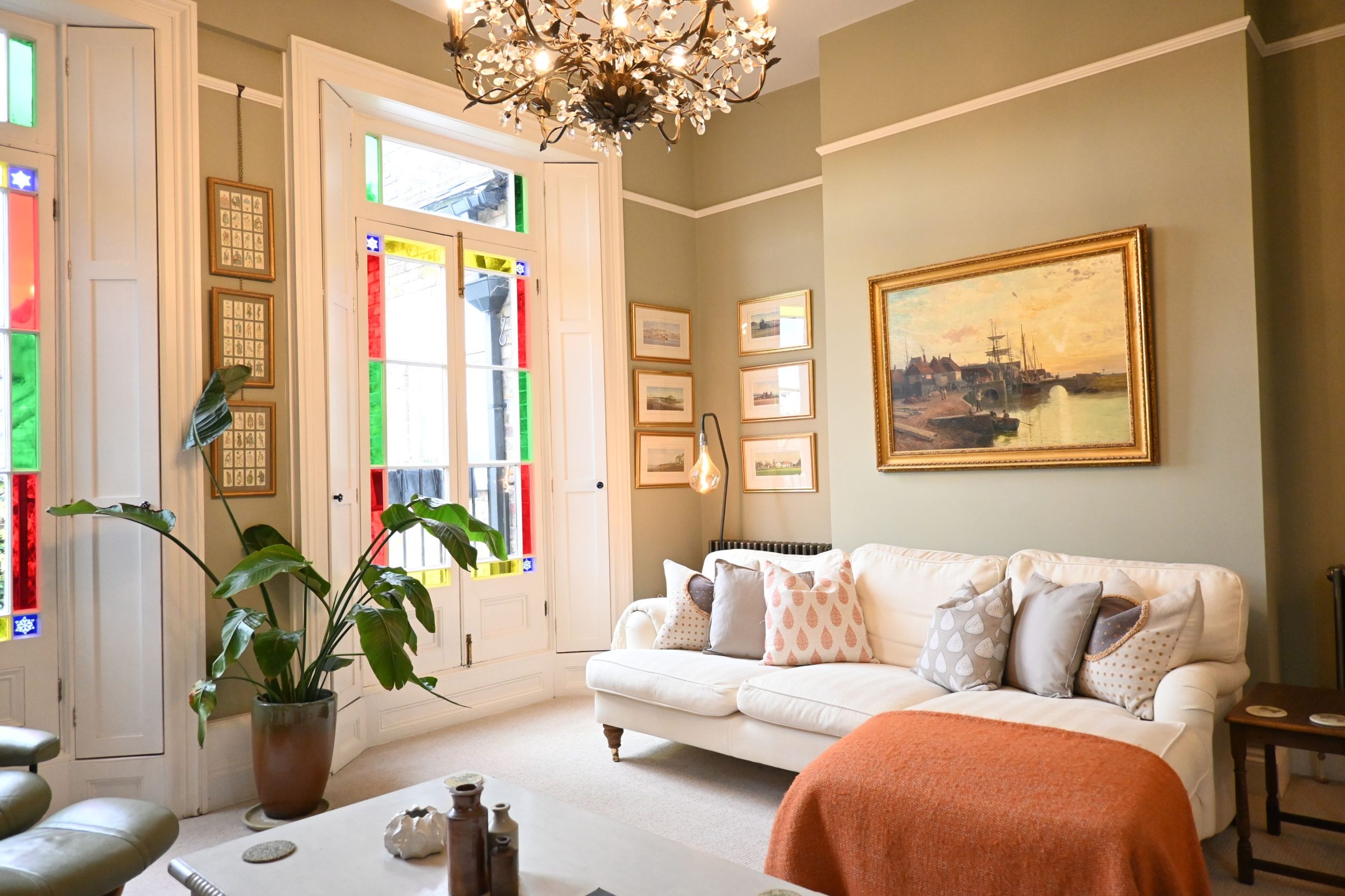 Your light-filled living space is framed by striking floor-to-ceiling windows, where soft pastel tones and comfortable seating create the perfect place to unwind after a day exploring Sandwich or the nearby coast.