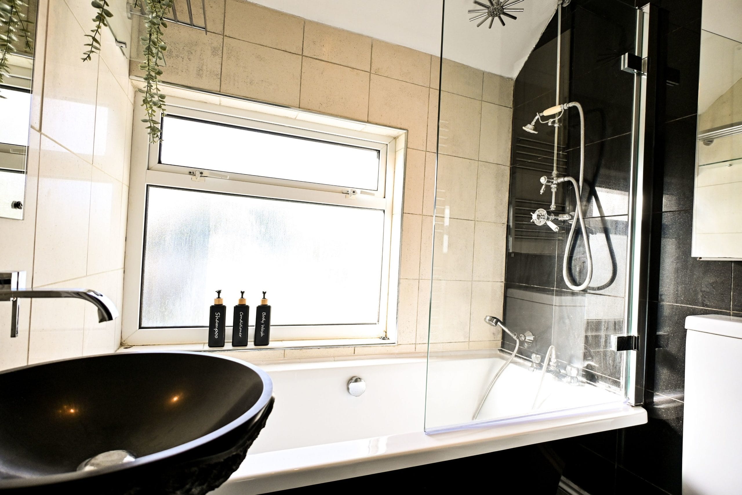 Enjoy a relaxing soak in the bathroom, where the bath sits beneath a window bringing in natural light, with a stylish black basin and contrasting fittings adding character.